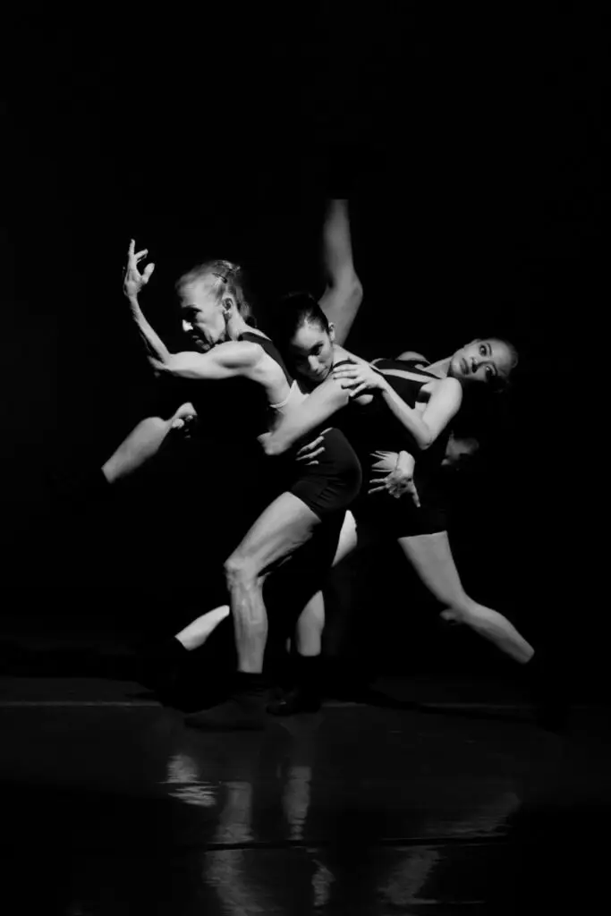 Dynamic black and white photo of a group of dancers performing contemporary choreography on stage.